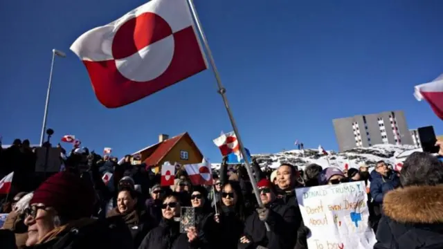 Em Nuuk, manifestantes da Groenlândia agitam bandeiras do país e exibem cartazes contra as intenções de Donald Trump.