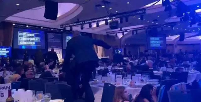 Imagem de grande salão de eventos com telões e pessoas ao redor de mesas